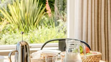 A table with a coffee pot, glasses, a pitcher, and a basket of fruit.