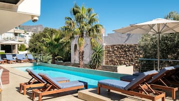 A poolside area with lounge chairs, a pool, palm trees, and a stone wall.