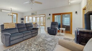 A spacious living room with a grey sofa, a patterned rug, a fireplace, and a ceiling fan.
