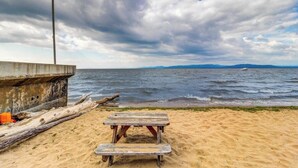 A beach with a wooden bench, a concrete structure, and a view of the sea and distant mountains.