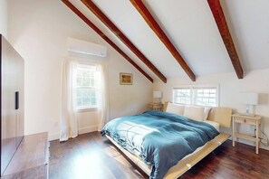 Een slaapkamer met een bed, houten balken, een raam en een nachtkastje.