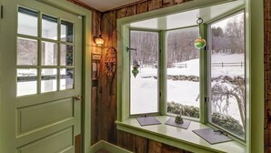 Ein Zimmer mit grüner Tür, einem Fenster mit Blick auf eine verschneite Landschaft und einer Wandleuchte.