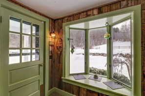 Ein Zimmer mit grüner Tür, einem Fenster mit Blick auf eine verschneite Landschaft und einer Wandleuchte.