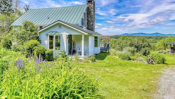 Ein Haus mit einem Steinkamin, einer Veranda und Blick auf die umliegende Landschaft.