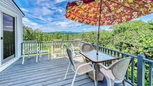 Eine Terrasse mit Tisch, Stühlen und Sonnenschirm, mit Blick auf Grünflächen und Berge.