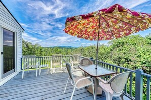 Eine Terrasse mit Tisch, Stühlen und Sonnenschirm, mit Blick auf Grünflächen und Berge.