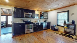 A kitchen with dark cabinets, stainless steel appliances, and a wooden floor. - Dog-friendly getaway with mountain views, games, & deck - near skiing & trails (Mount Holly)
