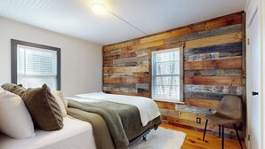 A bedroom with a wooden wall panel, a bed, a chair, and a window. - Dog-friendly getaway with mountain views, games, & deck - near skiing & trails (Mount Holly)