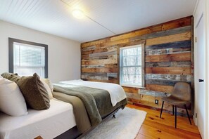 Ein Schlafzimmer mit Holzwandverkleidung, einem Bett, einem Sessel und einem Fenster.