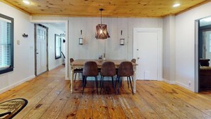 A dining area with a wooden table and chairs, a hanging light fixture, and a white door in the background. - Dog-friendly getaway with mountain views, games, & deck - near skiing & trails (Mount Holly)