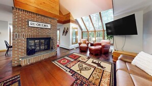 A spacious living room with a brick fireplace, leather sofas, a large TV, and a skylight. - Two-story condo with forest views, Echo Lake beach access, pool, dock & tennis (Plymouth)