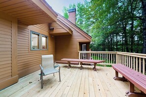 A wooden deck with a bench and a chair, a small table, and a railing.