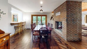 A dining area with a brick fireplace, wooden flooring, and a large window. - Two-story condo with forest views, Echo Lake beach access, pool, dock & tennis (Plymouth)