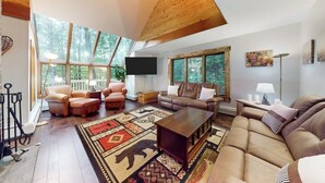 A spacious living room with a high ceiling, large windows, a flat-screen TV, leather sofas, and a patterned rug. - Two-story condo with forest views, Echo Lake beach access, pool, dock & tennis (Plymouth)