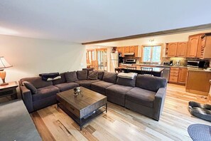 Ein modernes Wohnzimmer mit einem Ecksofa, einem Holztisch und einer Küche im Hintergrund.