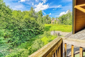 Eine Holzterrasse mit Blick auf eine üppige grüne Landschaft, in der Ferne ein Haus.