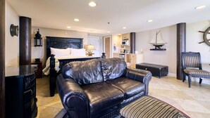 Una habitación de hotel moderna con sofá de cuero, cama con cabecera oscura, una pequeña cocina y decoración náutica.