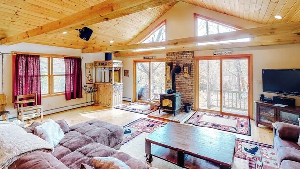 A spacious living room with a fireplace, wooden ceiling beams, a television, and a large window.