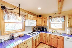 A kitchen with wooden cabinets, a white microwave, a stove, and a sink. - Two-story, dog-friendly house (Wardsboro)