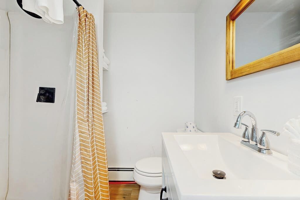 A bathroom with a shower curtain, a toilet, a sink with a mirror, and a light switch.