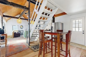 Un vaste loft doté d’un plafond en bois, d’un escalier, d’un coin cuisine et d’un espace repas.