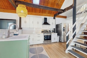 Une cuisine moderne avec des meubles blancs, un réfrigérateur en acier inoxydable et un escalier en bois.
