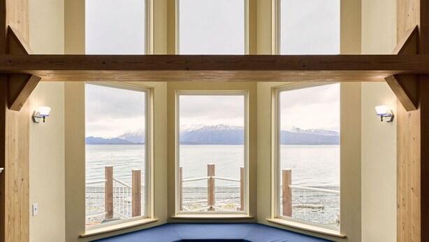 Ein Eckzimmer mit eingebauter Bank, großen Fenstern und Blick auf einen See und Berge.