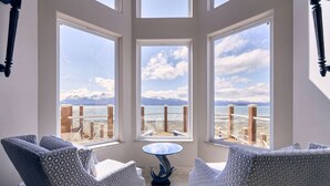A room with three large windows, a round table, and two patterned chairs.