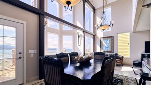 A dining area with a large table, multiple chairs, and a view of the sea through large windows.