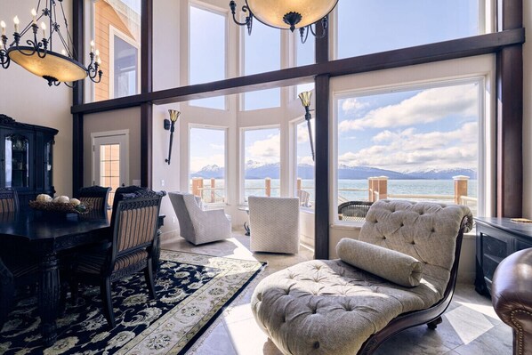 A spacious room with a large window overlooking a scenic mountain view, a dining area with a dark wooden table and chairs, and a plush armchair.
