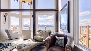 A spacious room with large windows, a leather armchair, a tufted ottoman, and a patterned rug.