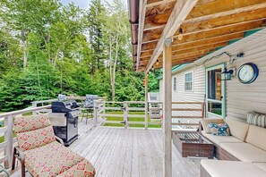 Eine überdachte Terrasse mit Gartenmöbeln, einem Grill und Blick auf eine Hütte.