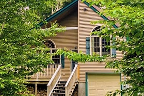 Ein zweistöckiges Haus mit Veranda, Garage und Treppe zum zweiten Stock.