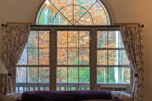 Ein Zimmer mit einem großen Bogenfenster, einem Bett mit violetter Decke und Vorhängen mit floralem Muster.