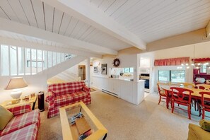 Amplia sala de estar con un sofá rojo a cuadros, una mesa de centro de madera y un comedor con sillas rojas.