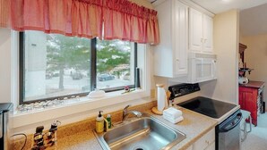 A kitchen with a window, stainless steel sink, white cabinets, and a red valance.