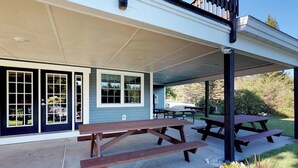 A covered patio area with picnic tables and a building with large windows and a door.