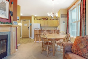 A cozy dining area with a wooden table and chairs, a fireplace, and a sofa with a patterned cushion. - Mountain Home w/Balcony, Pool Views, Shared Pool, Hot Tub, Free WiFi, Fireplace (Stratton)