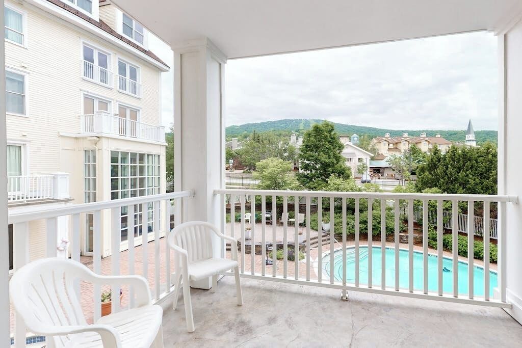 Un balcon avec des chaises blanches, une piscine et une vue sur un quartier résidentiel avec des maisons et des arbres.