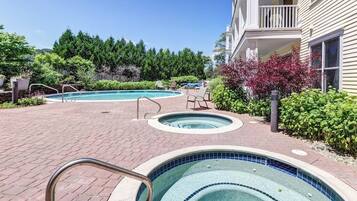 Un espace piscine comprenant un jacuzzi, des chaises longues et un bâtiment doté d’un balcon.
