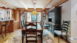 Un comedor con una mesa y sillas de madera, una araña y vistas al exterior a través de amplios ventanales.