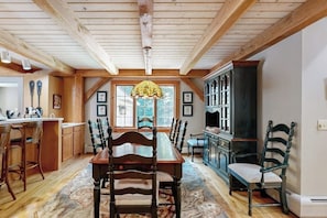 A dining area with a wooden table and chairs, a chandelier, and a view of the outdoors through large windows. - Tree-lined lodge with deck, fireplaces, porch, game room, & fast WiFi (Peru)