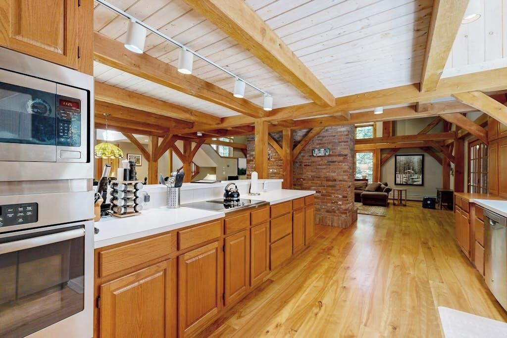 A spacious kitchen with wooden beams, a brick wall, and modern appliances.