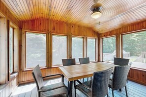 A wooden-paneled room with a table and chairs, large windows, and a ceiling fan. - Tree-lined lodge with deck, fireplaces, porch, game room, & fast WiFi (Peru)
