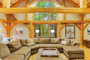 A large, L-shaped sectional sofa in a room with exposed wooden beams and a large window. - Tree-lined lodge with deck, fireplaces, porch, game room, & fast WiFi (Peru)