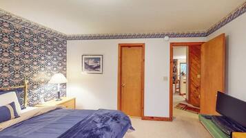 A bedroom with a bed, a nightstand, a lamp, a television, and a door leading to another room.