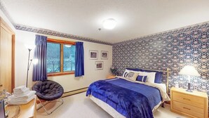 A bedroom with a bed, a chair, a desk, a lamp, and a window with curtains.