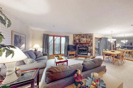 A living room with a sofa, a television, a fireplace, and a dining area with chairs and a table.