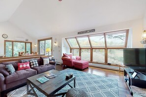 Ein modernes Wohnzimmer mit großem Fenster, einer Couch, einem Couchtisch und einem Fernseher.