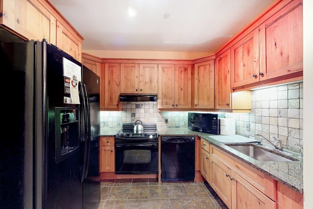 A kitchen with wooden cabinets, a black refrigerator, a stove, a microwave, and a dishwasher.